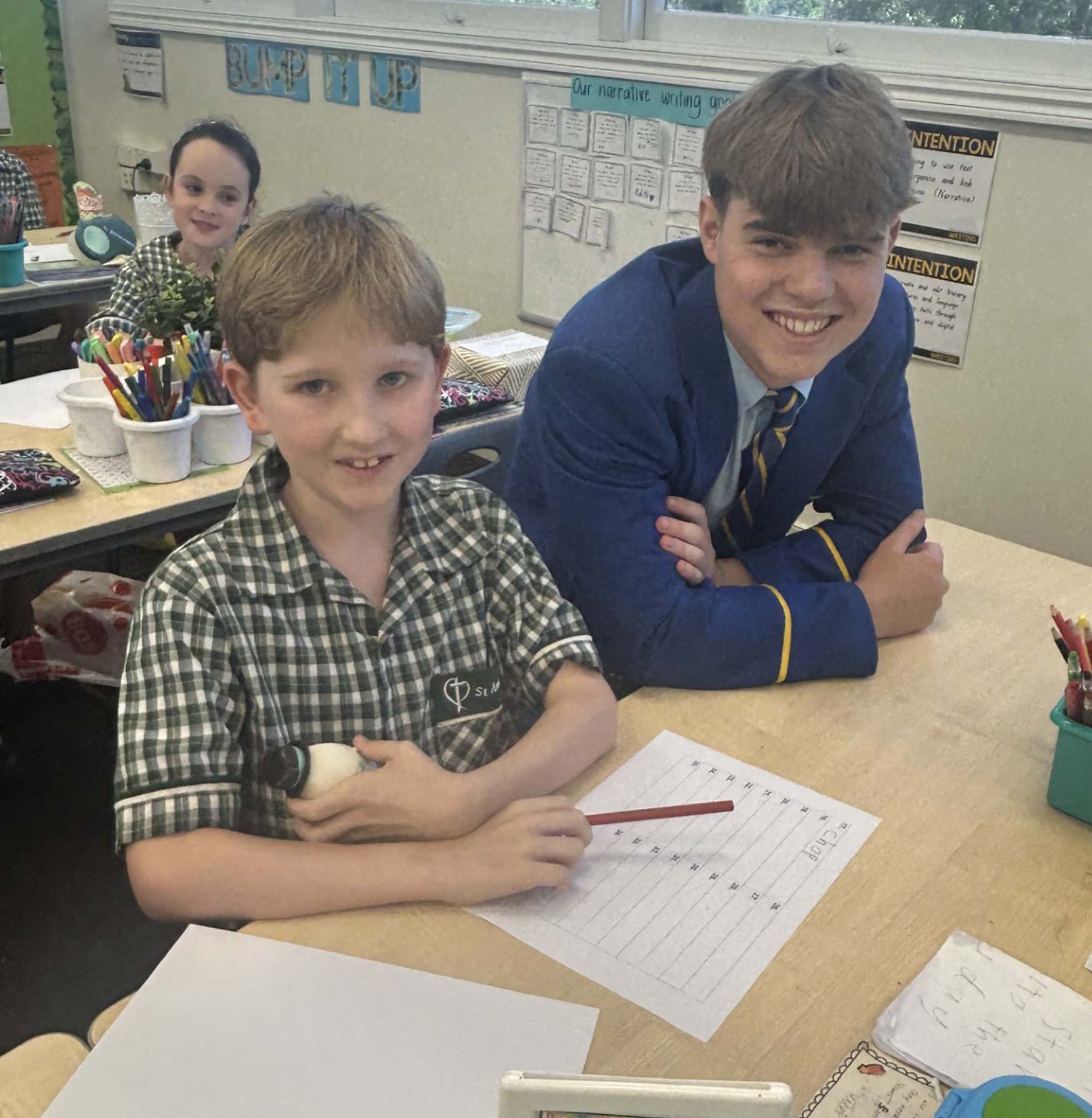 Older student assisting a younger student during a classroom task, highlighting leadership, learning partnerships and student connection